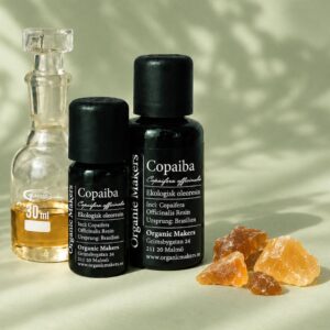Ekologisk Copaiba oleoresin i uv-skyddande glasflaskor bredvid en glaskaraff med olja, med bitar av copaibakåda