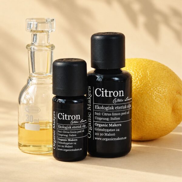 Ekologisk eterisk olja Citron i uv-skyddande glasflaskor bredvid en glaskaraff med olja, med en hel citron