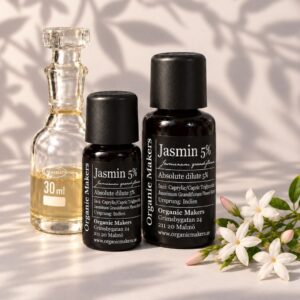 Jasmin absolut 5% i uv-skyddande glasflaskor bredvid en glaskaraff med olja, med vita jasminblommor