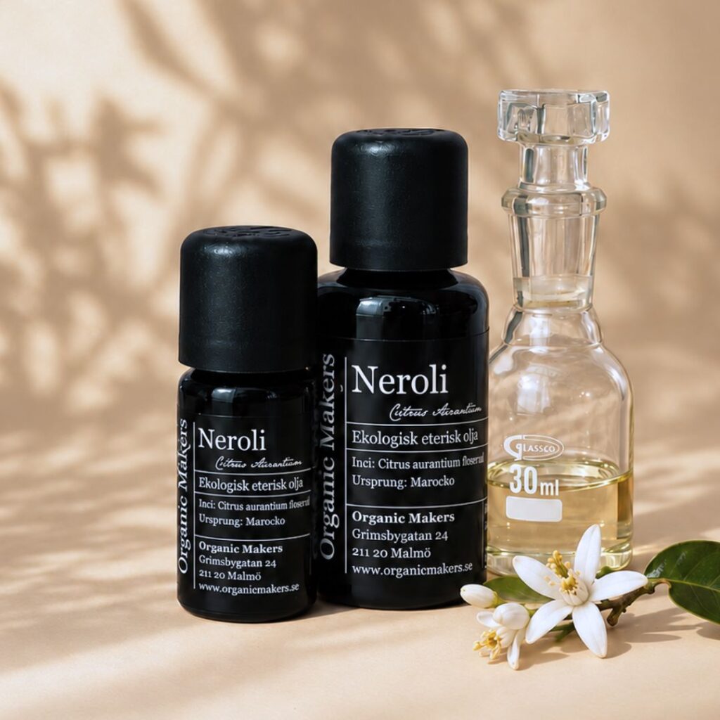 Ekologisk eterisk olja Neroli i uv-skyddande glasflaskor bredvid en glaskaraff med olja, med vita apelsinblommor
