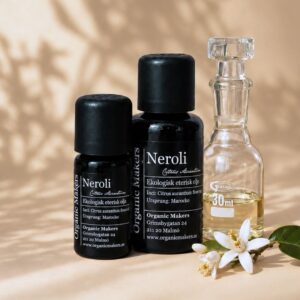 Ekologisk eterisk olja Neroli i uv-skyddande glasflaskor bredvid en glaskaraff med olja, med vita apelsinblommor