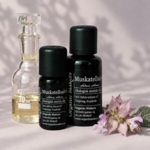 Ekologisk eterisk olja Muskatellsalvia i uv-skyddande glasflaskor bredvid en glaskaraff med olja, med muskatellsalviablommor