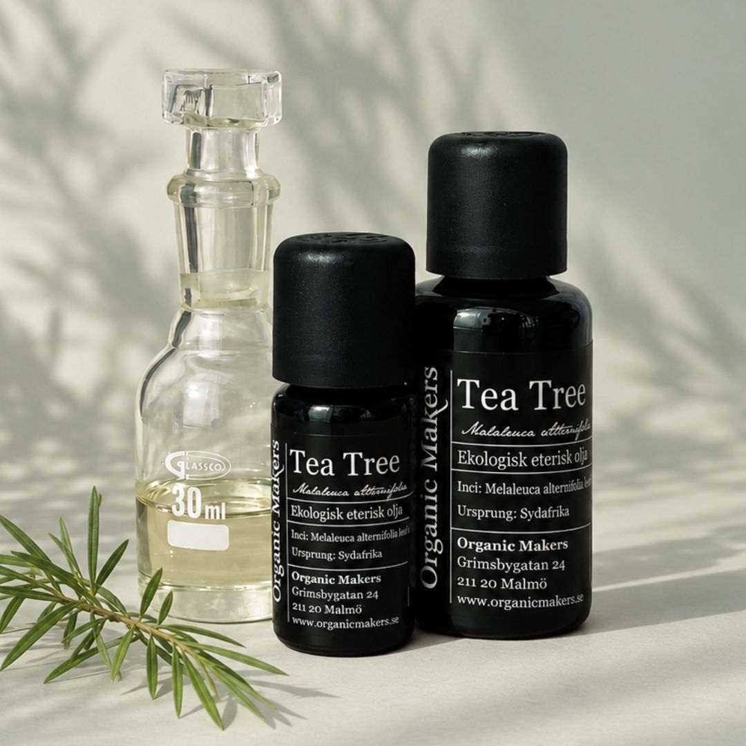 Ekologisk eterisk olja Tea Tree i uv-skyddande glasflaskor bredvid en glaskaraff med olja, med en kvist tea tree