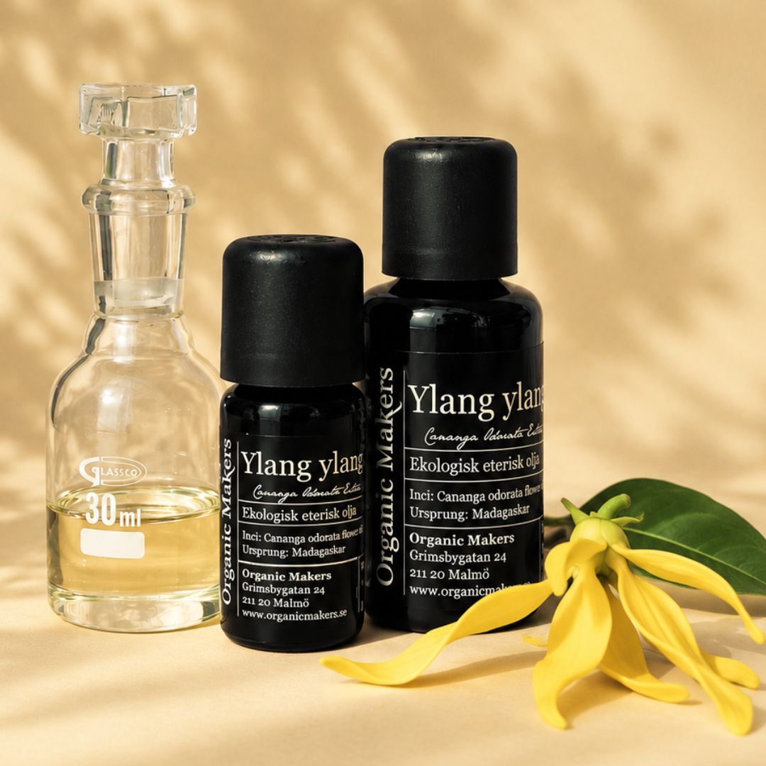 Ekologisk eterisk olja Ylang Ylang i uv-skyddande glasflaskor bredvid en glaskaraff med olja, med gula ylang ylang-blommor